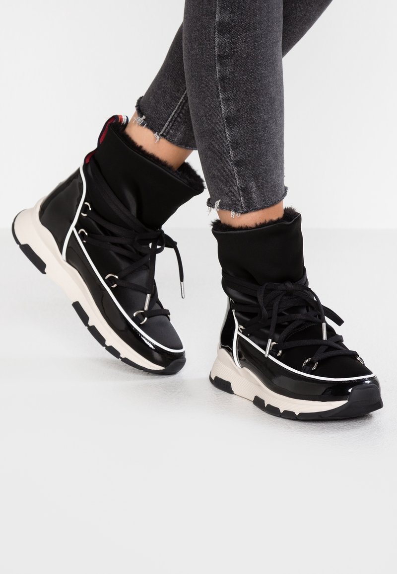 Czarne syntetyczne buty z wyściełanym kołnierzem, białymi akcentami i grubymi podeszwami. Widoczna teksturowana tkanina i sznurówki, design zawiera metaliczne elementy.