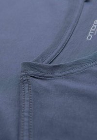 Camiseta de algodón azul con cuello redondo, bordes acanalados y detalles de costura visibles. Textura de tela suave con un acabado liso.