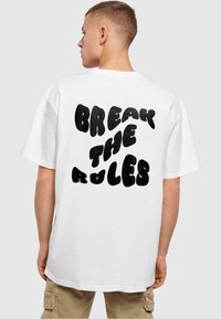 Hvid T-shirt med en dristig sort grafisk tekstprint på ryggen, der siger "BREAK THE RULES", lavet af bomuld med en afslappet pasform.