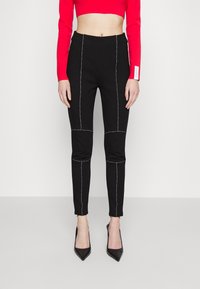 Zwarte fitted broek met contrasterende witte stiksels, taps toelopende pijpen en een elastische tailleband, gecombineerd met een rode cropped longsleeve en zwarte hakken.