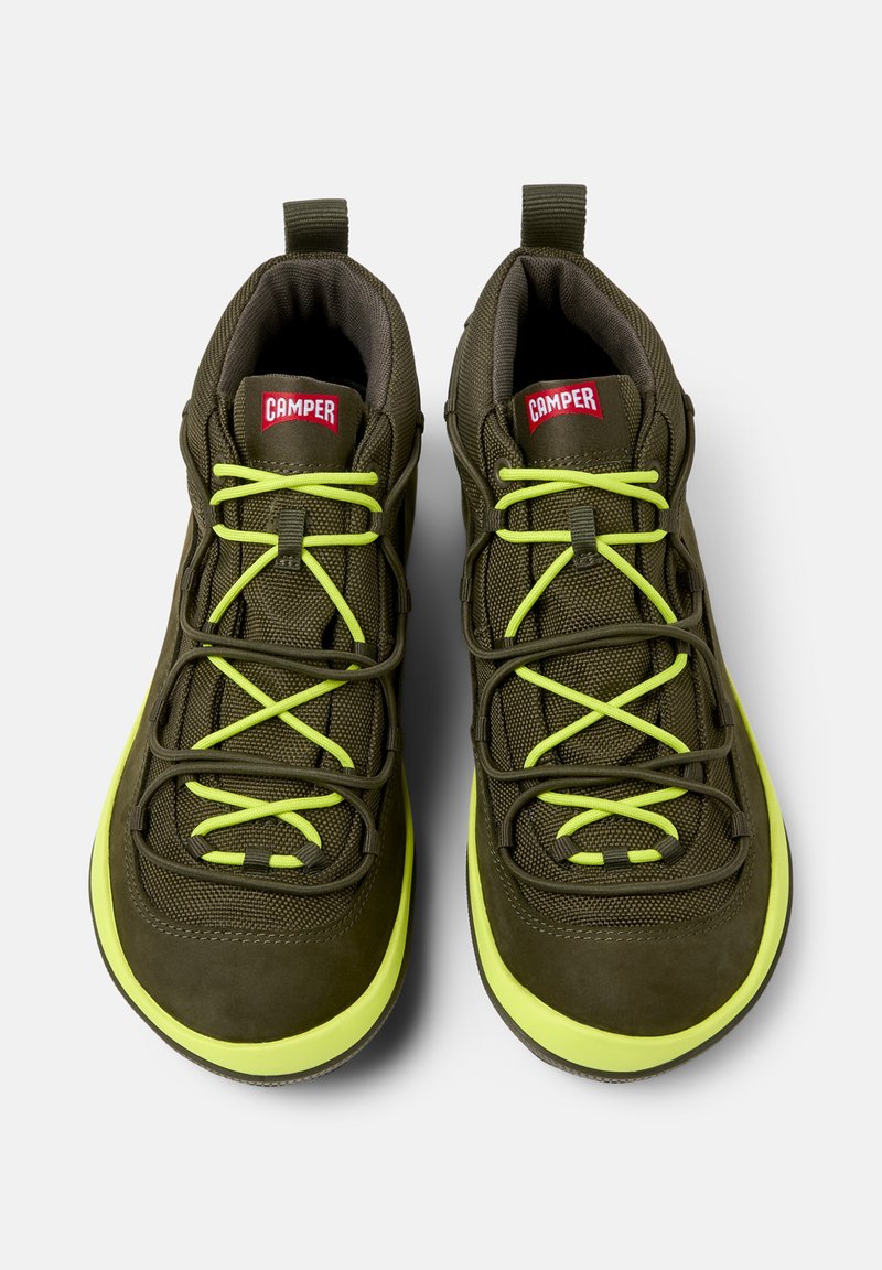 Olijf groene sportschoenen met felgele veters, met een Camper-logo op de tong, weergegeven vanuit een bovenaanzicht.
