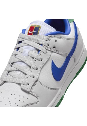 Sneaker en cuir blanc avec un swoosh Nike bleu, des lacets gris, une semelle verte et un patch logo multicolore sur la languette en mesh blanc.
