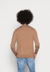 Maglione a maniche lunghe marrone in maglia con collo rotondo e texture a coste, indossato da una persona di spalle, abbinato a jeans azzurri chiari.