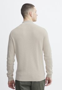 Pull en tricot beige avec un motif à côtes texturé, manches longues et coupe confortable, présenté de dos.