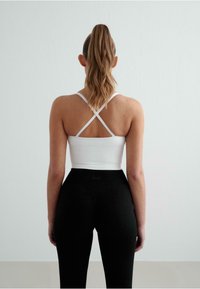 Hvid cropped tanktop med krydsede stropper og en glat tekstur, parret med højtaljede sorte leggings. Enkel og funktionel design.