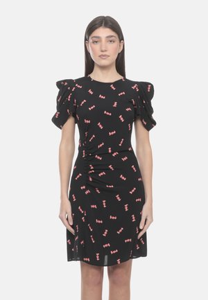 Donna che indossa un vestito nero con motivi di caramelle rosa, maniche corte a sbuffo e dettaglio arricciato sul lato sinistro della vita.