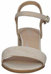 Sandali con tacco alto in suede beige con una larga fascia anteriore e una fascia alla caviglia regolabile con fibbia in tono oro. Soletta perforata per una maggiore traspirabilità.