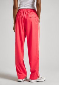 Pantaloni sportivi rosa brillante con vestibilità rilassata, vita elastica e strisce laterali. Presentano una tasca sul retro con dettaglio bottone.