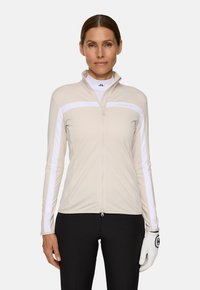 Giacca beige con zip, dettagli bianchi, maniche lunghe e design aderente. Realizzata in materiale liscio e elasticizzato. Include un colletto alto e dettaglio del logo.