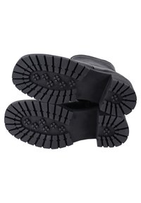 Musta kuminen kengänpohja, jossa on syvät urat, leveät reunat ja pyöreät kuviot liukastumisen estämiseksi. Sileä yläreuna ja kestävä rakenne.