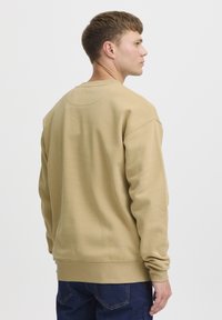 Beige-sviiter, millel on ümmargune kaelus, pikad varrukad ning soonikud mansettides ja allservas. Kangas näeb välja pehme ja kergelt struktureeritud.