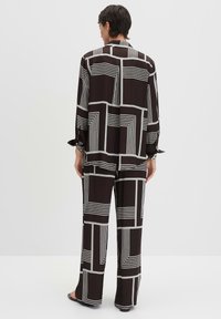 Zwart-wit gestreepte lounge-outfit met een colbert met lange mouwen en een losse broek, beide met geometrische ontwerpen.