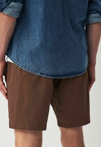 Brune shorts i ensfarvet design, lavet af en blanding af bomuld, har lige kanter og en afslappet pasform, parret med en denim skjorte med knapper.