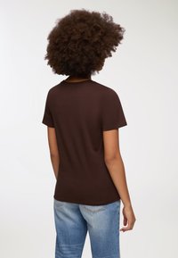 Brązowa koszulka z krótkim rękawem, o okrągłym dekolcie, wykonana z gładkiej bawełny. Nosi się ją z jasnoniebieskimi dżinsami o klasycznym kroju.