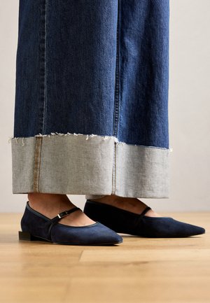 Tumesuede Mary Jane nelgid, millel on rihm, on kokku sobitatud heledate denimpükstega, millel on kulunud heledate denimi servade rõhutamiseks. Puitpõranda taust.