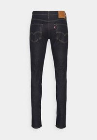 Jeans de ganga de lavagem escura com um ajuste justo, costura laranja contrastante, e dois bolsos traseiros com um design curvado distinto. Patch de couro castanho na cintura.