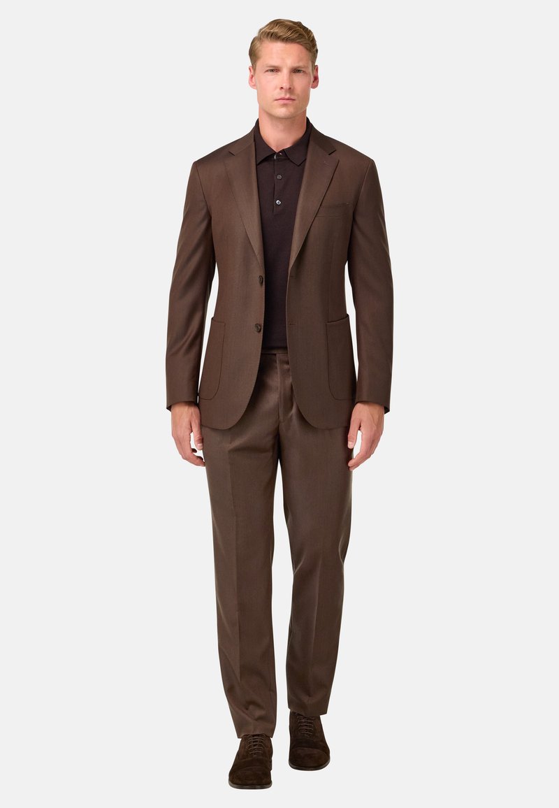 Brūns uzvalks ar pielāgotu piegriezumu, vienas rindiņas žakete un divas priekšējās kabatas, apvienots ar tumšu polo kreklu un brūnām kurpēm.