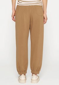 Bruine joggers van zachte stof hebben een taps toelopend ontwerp, elastische boorden, een achterzak en een gladde textuur voor comfort.