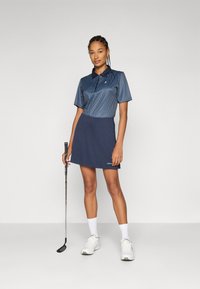 Tengeri kék golfruha csíkozott, rövid ujjú póló felsőrésszel és egyszínű szoknyával. Jellemzői közé tartozik a gallér, a logó részlet, valamint golfütő és cipő mellé párosítva.