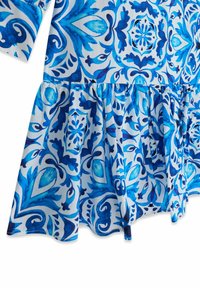 Section de robe avec taille froncée présentant des motifs floraux et géométriques bleus et blancs complexes sur un tissu léger.