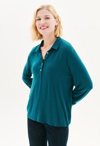 Tummansininen pitkähihaisen polo-paita, jossa on napitettava kaulus, rento malli ja kevyet kankaat. Huomiota herättävät kultaiset napit koristelevat nappilistaa.