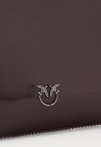 Glatka tamnosmeđa burgundska torbica sa teksturiranom površinom, koja sadrži srebrno ukrašavanje u obliku dva ptica i kružne osnove.