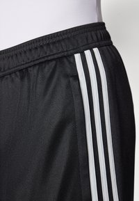 Zwarte sportieve shorts van gladde stof hebben drie witte strepen langs de zijkant, een elastische tailleband en een ontspannen pasvorm.