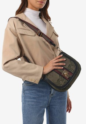 Green fabric crossbody bag with embossed design, dark trim, gold hardware, and a maroon striped adjustable strap. Worn at the hip.
