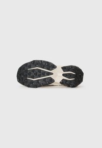 Black rubber outsole with a textured grip pattern, midsole in light cream color; designed for traction and durability in outdoor activities.
