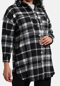 Chemise boutonnée à carreaux noir et blanc avec des manches longues, col classique, fentes latérales et coupe décontractée. Tissu en mélange de laine texturé.