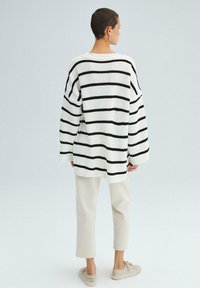 Pull en tricot blanc surdimensionné avec des rayures noires, épaules tombantes, ourlet côtelé, assorti à un pantalon beige court et des baskets légères.
