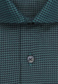 Groen en marineblauw patroonstof met een hondentandmotief, voorzien van een grijze knoop en een puntige kraag. De gestructureerde weving voegt diepte toe.