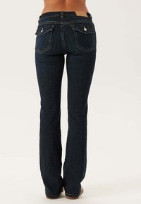 Ciemnoniebieskie dżinsy typu bootcut z średnim stanem, dwoma tylnymi kieszeniami i subtelnymi detalami przeszycia. Gładka faktura z drobnym wyblaknięciem.