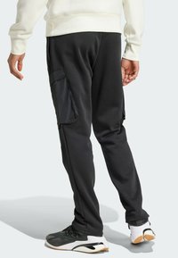 Black sweatpants with a tapered fit, featuring a shiny black cargo pocket on the left side and elastic cuffs at the ankles, paired with athletic shoes.