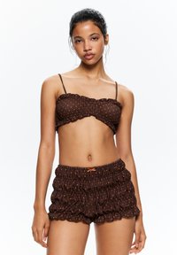 Brown polka dot bikini top with ruffles and adjustable straps, paired with matching ruffled shorts featuring an orange accent tie.