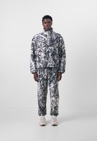 Fleece pullover and pants set with a black and white abstract pattern, featuring a high collar, zipper, and textured fabric. Paired with light sneakers.