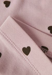 Hellrosafarbener Stoff mit glatter Textur, der mit kleinen schwarzen Herzenmuster verziert ist. Sichtbare Nähte und eine gefaltete Kante.