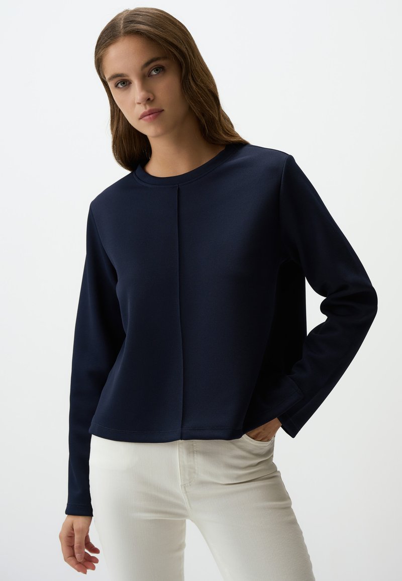 Maglietta a maniche lunghe blu navy con scollo rotondo, caratterizzata da un dettaglio cucitura frontale e una vestibilità rilassata, indossata sopra jeans chiari.