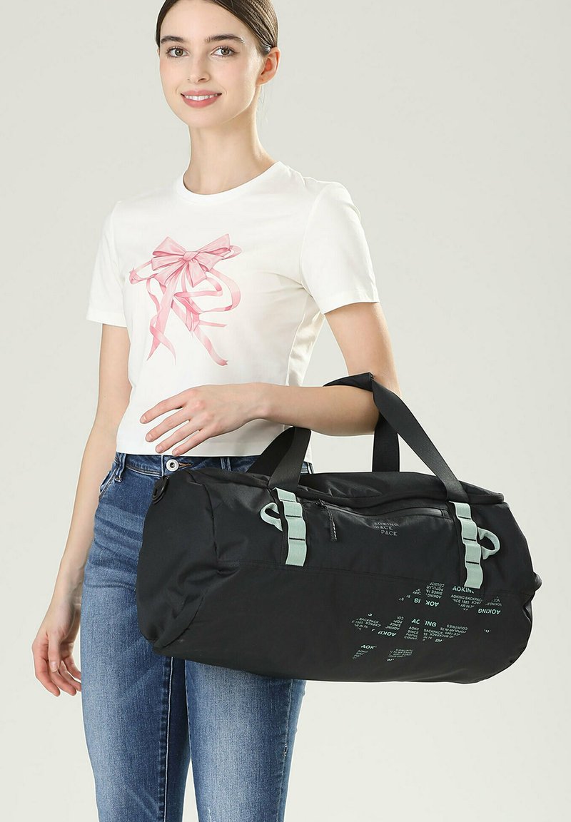 Sac de sport noir avec des sangles et des accents vert menthe. Comprend une poche zippée sur le côté et des détails textuels imprimés. Fabriqué en matériau durable.