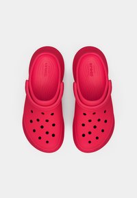 Tamancos vermelhos de borracha com design perfurado, apresentando uma tira traseira e uma palmilha texturizada para conforto. Sem adornos adicionais.