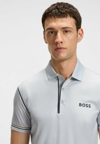 Polo shirt grigio chiaro con maniche corte, tessuto testurizzato, dettagli neri lungo il colletto e i bordi delle maniche, e logo ricamato "BOSS".