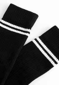 Schwarze Socken mit gerippter Textur, die oben zwei weiße Streifen haben. Das Material wirkt weich und dehnbar. Ideal für die Freizeit.