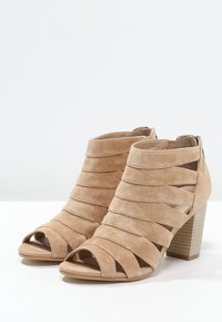 Beige nubuck avokadot, joissa on viisto leikattu yläpinta ja pinottu korko. Varustettu sivuzipperillä helppoa pukemista varten.