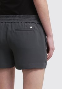 Grijze shorts met elastische taille en een gladde textuur, voorzien van twee achterzakken en een klein detail van zilverkleurig beslag.