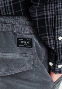 Grijze corduroy broek met een gestructureerd oppervlak, voorzien van een achterzak en een zwart etiket met de tekst "REPLAY PREMIUM SELECTION."