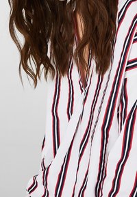 Blusa bianca con strisce verticali rosse e blu navy. Vestibilità ampia con scollatura a V e un tessuto leggero e testurizzato.