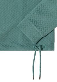 Nära bild av en teal-färgad texturerad sweatshirtärm och nederkant med justerbar dragsko som har metallaglets.