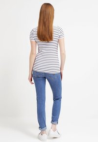 Camiseta a rayas ajustada en blanco y marino, combinada con jeans azul claro con dobladillos enrollados y zapatillas blancas, vista desde la parte de atrás.