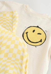 Katoenen sweatshirt in crème met een zwart-gele smiley graphic, gecombineerd met gele geruite stof met een ribbeltextuur.