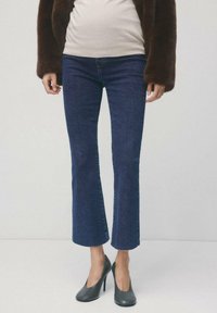 Marineblauwe jeans met wijde pijpen in denim met een gladde textuur. Gecombineerd met zwarte hoge hakken met een puntige neus.